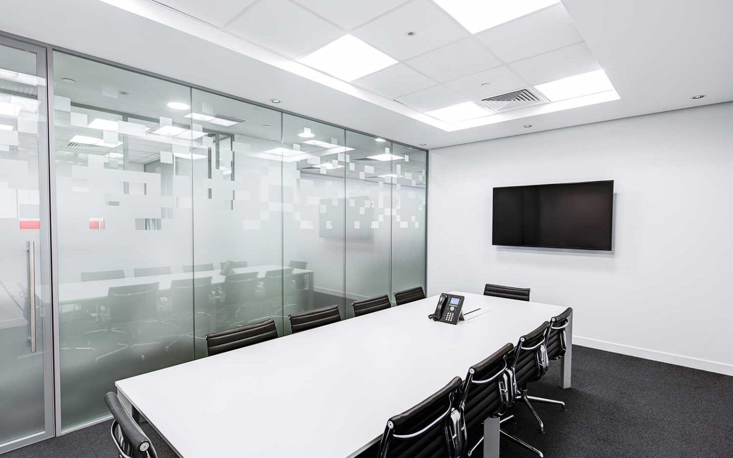 boardroom with long table and 10 office chairs neatly tucked under the table. Large tv is mounted on the wall.